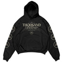 Black Thousand Below hoodie featuring premium Shaka Wear material, a geometric mountain and band logo on the front, plus circular mountain logos running down each sleeve—an eye-catching printed garment.