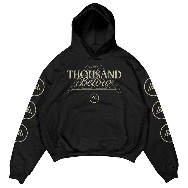Black Thousand Below hoodie featuring premium Shaka Wear material, a geometric mountain and band logo on the front, plus circular mountain logos running down each sleeve—an eye-catching printed garment.