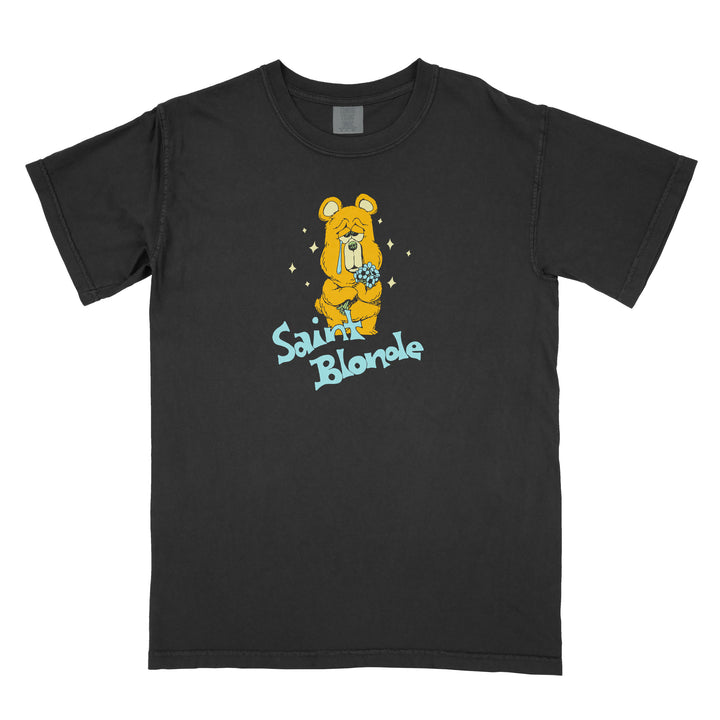 This black Saint Blonde t-shirt features a comfort colors design with a printed sad yellow bear holding a blue ball, sparkles, and “Saint Blonde” in light blue stylized letters below the illustration.