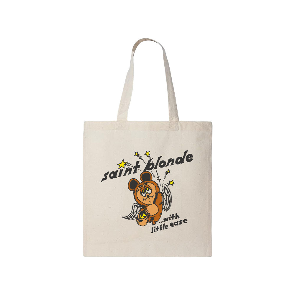 Saint Blonde beige tote bag with a winged bear and star illustration. Features "saint blonde" and "with little ease" in stylized fonts. Available for presale now—shipping begins 7/3/26.