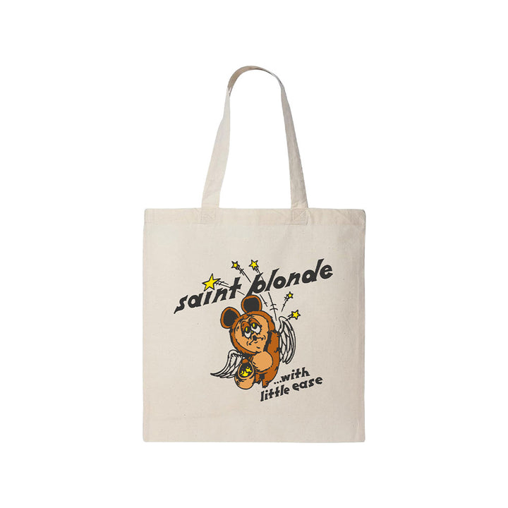 Saint Blonde beige tote bag with a winged bear and star illustration. Features "saint blonde" and "with little ease" in stylized fonts. Available for presale now—shipping begins 7/3/26.