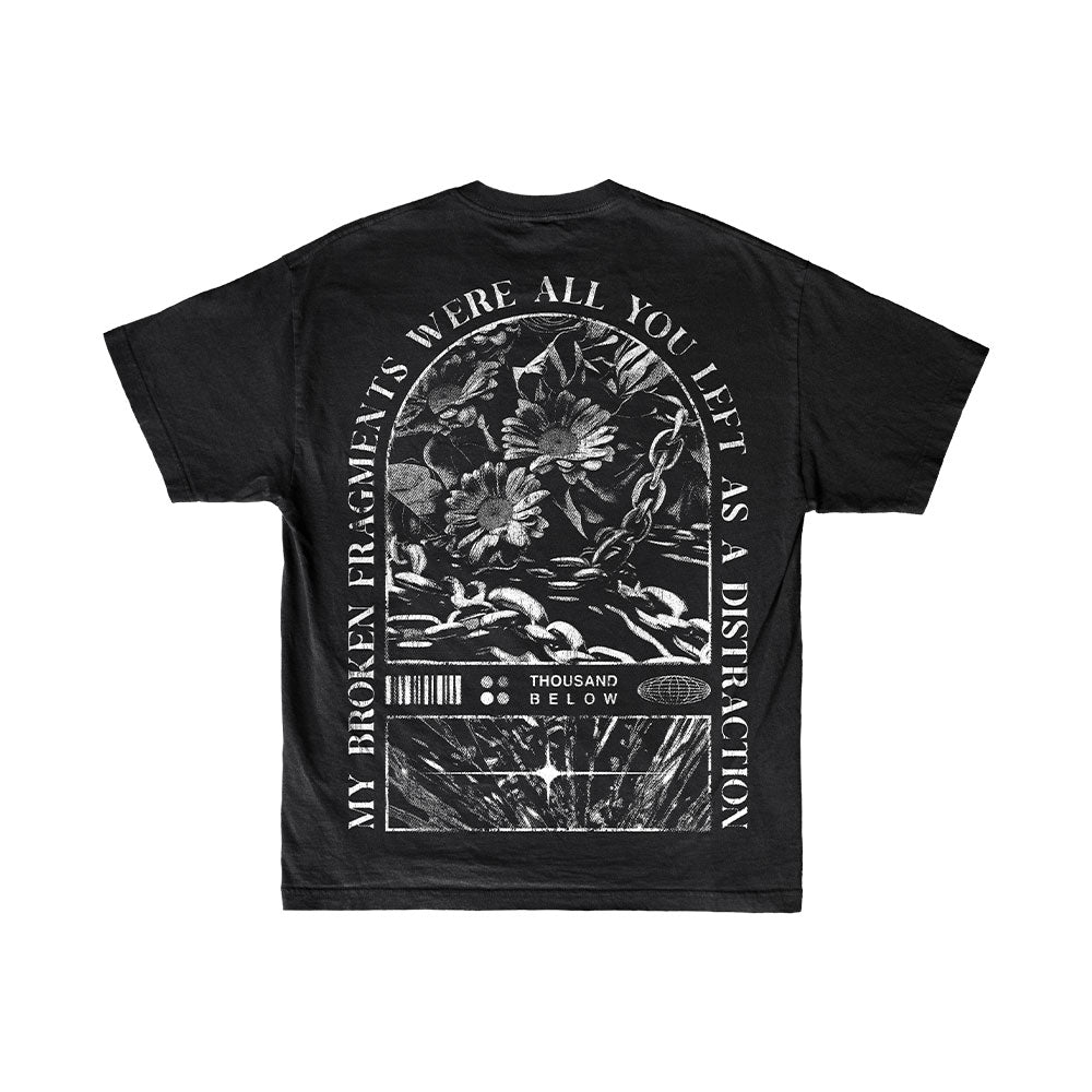 Black T-shirt by Thousand Below featuring a bold white graphic of flowers, crescent moon, and barcodes, with the encircled text: "My broken fragments were all you left as a distraction.